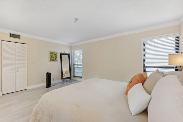 bedroom with crown molding, light hardwood / wood-style flooring, a textured ceiling, and a closet