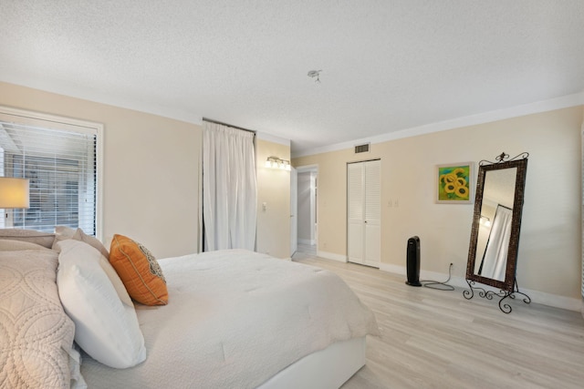 bedroom featuring a closet, a textured ceiling, light wood-type flooring, and crown molding