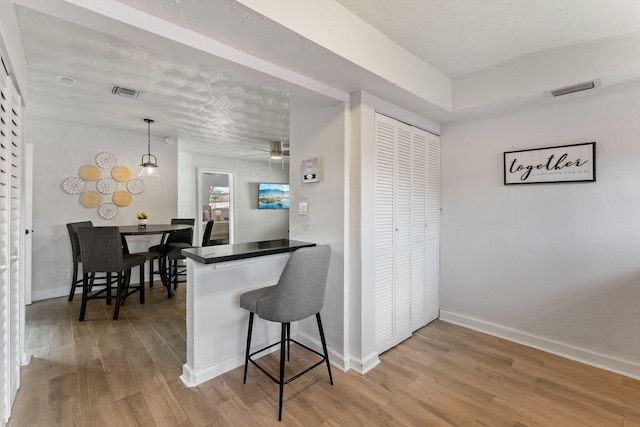 kitchen with a breakfast bar area, hanging light fixtures, kitchen peninsula, light wood-type flooring, and ceiling fan