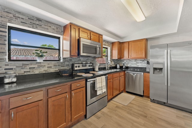 kitchen featuring decorative backsplash, appliances with stainless steel finishes, a textured ceiling, light wood-type flooring, and sink