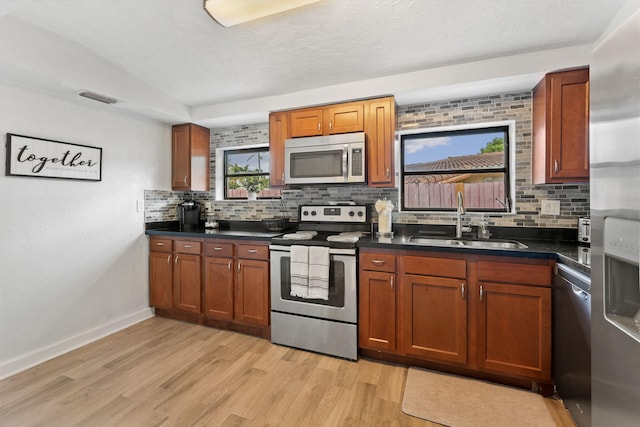 kitchen with appliances with stainless steel finishes, sink, backsplash, and light hardwood / wood-style floors