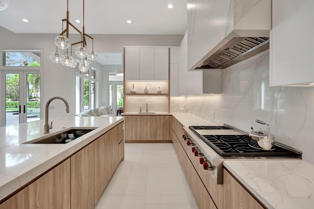 kitchen with decorative backsplash, white cabinets, premium range hood, stainless steel gas stovetop, and sink