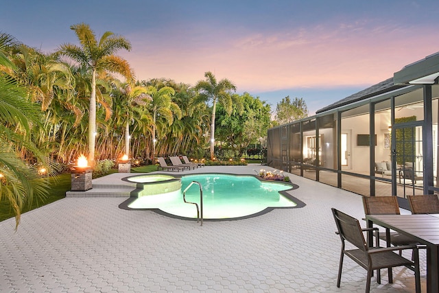 pool at dusk with glass enclosure, a patio area, and an in ground hot tub