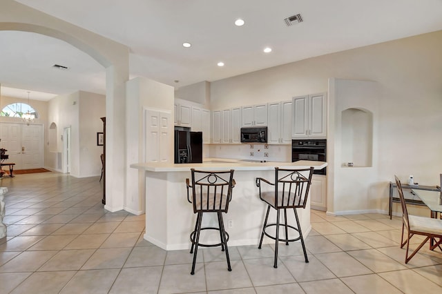 kitchen featuring black appliances, light tile patterned floors, a kitchen breakfast bar, and a kitchen island with sink