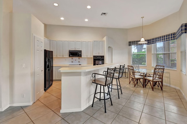 kitchen with decorative backsplash, black appliances, pendant lighting, light tile patterned floors, and white cabinets