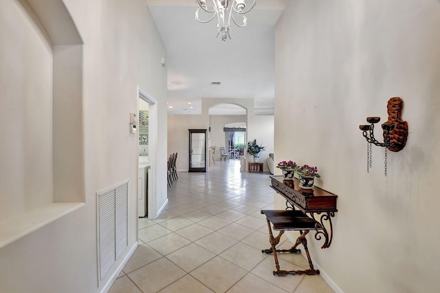 corridor with washer / clothes dryer, a notable chandelier, a towering ceiling, and light tile patterned flooring