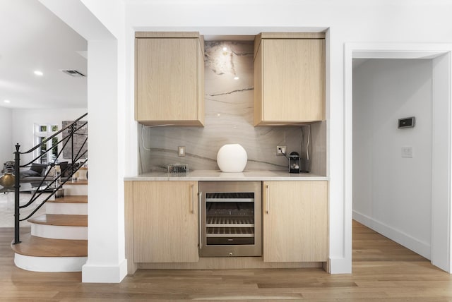 bar with light brown cabinetry, light wood-type flooring, wine cooler, and backsplash