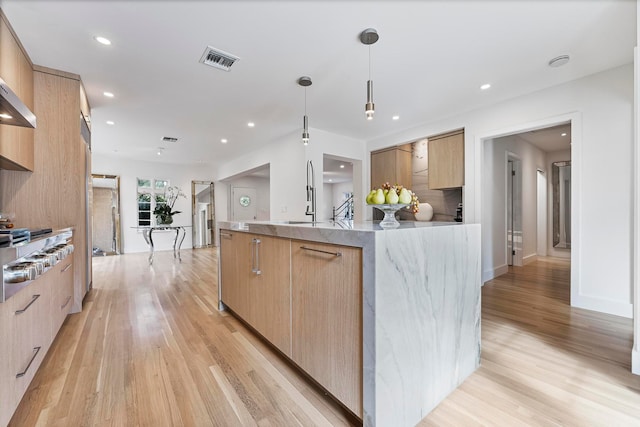 kitchen with light brown cabinetry, a center island with sink, and hanging light fixtures