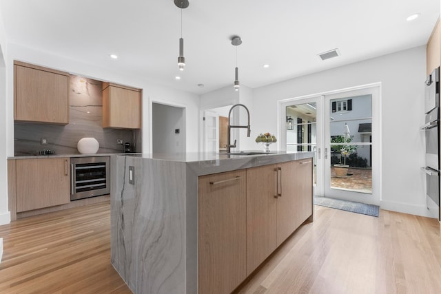 kitchen with a center island with sink, sink, hanging light fixtures, light hardwood / wood-style floors, and beverage cooler