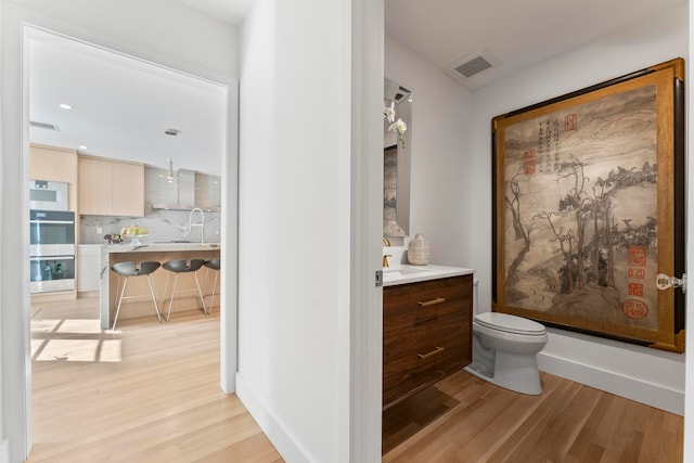 bathroom with hardwood / wood-style flooring, decorative backsplash, toilet, and vanity