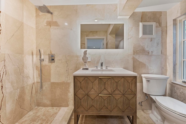 bathroom featuring tiled shower, vanity, toilet, and tile walls