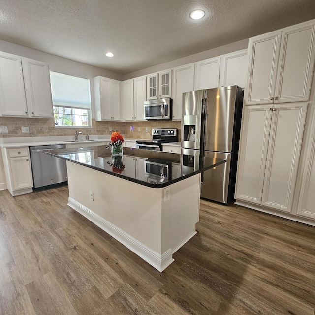 kitchen featuring stainless steel appliances, a sink, white cabinetry, a center island, and glass insert cabinets