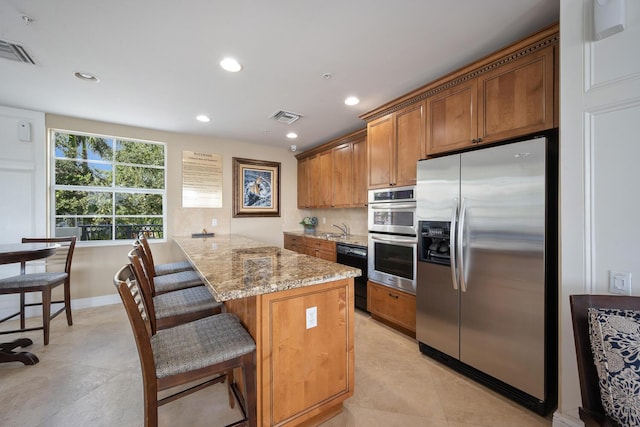 kitchen featuring tasteful backsplash, visible vents, appliances with stainless steel finishes, brown cabinets, and light stone countertops