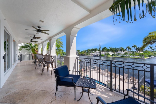 balcony with outdoor dining area, a water view, and a ceiling fan