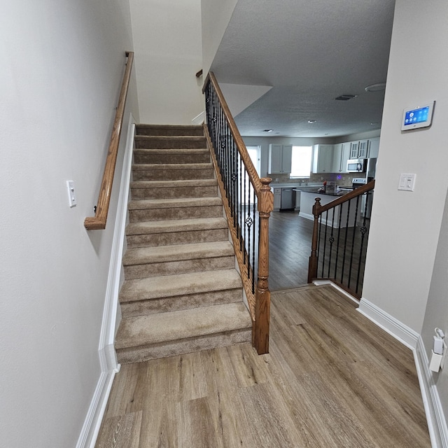 stairs with wood finished floors, visible vents, and baseboards