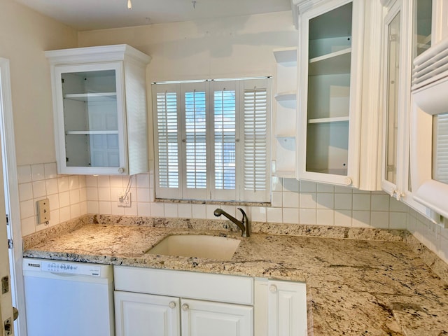 kitchen with sink, backsplash, white cabinetry, white dishwasher, and light stone countertops