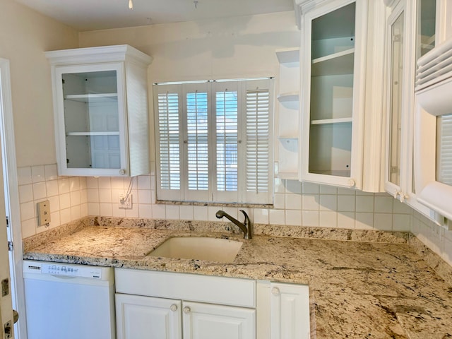 kitchen with sink, white dishwasher, white cabinetry, light stone counters, and decorative backsplash