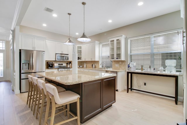 kitchen with a kitchen island, hanging light fixtures, stainless steel appliances, white cabinets, and decorative backsplash