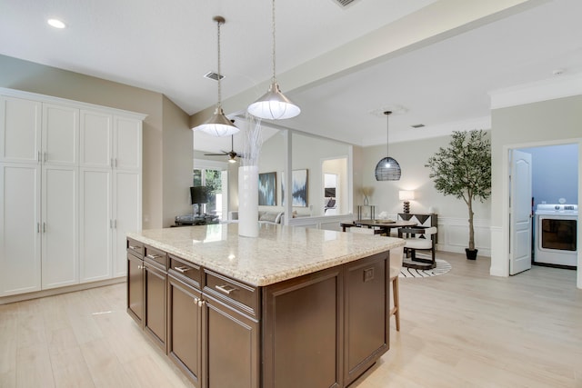 kitchen with washer / dryer, a center island, hanging light fixtures, ceiling fan, and light hardwood / wood-style flooring