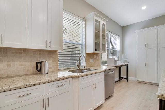 kitchen featuring white cabinets, light stone countertops, stainless steel dishwasher, light wood-type flooring, and sink