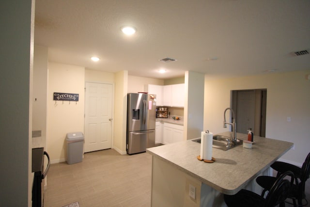 kitchen with white cabinets, an island with sink, a breakfast bar, stainless steel refrigerator with ice dispenser, and sink