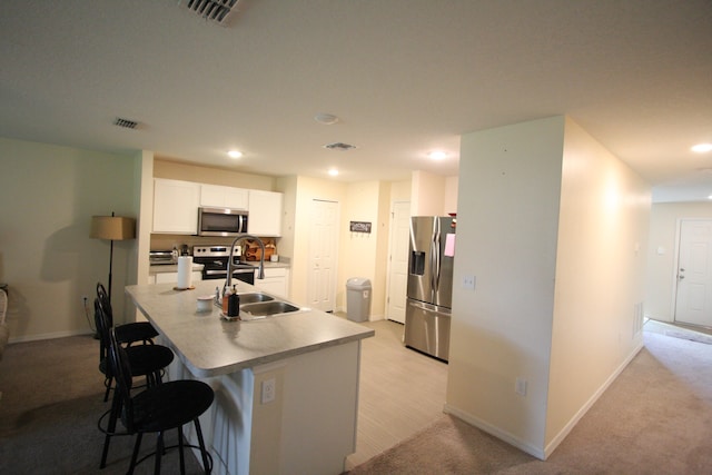 kitchen featuring a kitchen bar, an island with sink, white cabinetry, light carpet, and stainless steel appliances