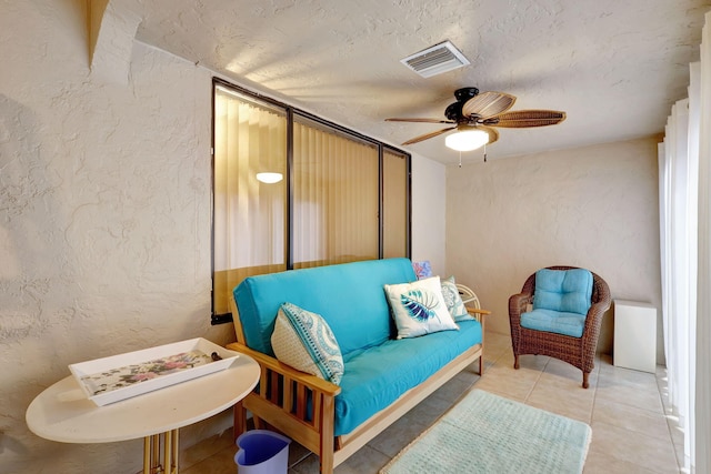 sitting room with visible vents, ceiling fan, and a textured wall