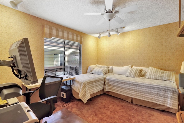 carpeted bedroom with wallpapered walls, track lighting, a ceiling fan, and a textured ceiling