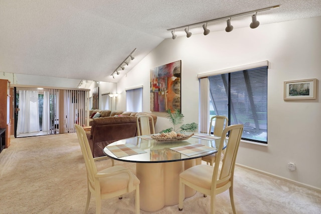 dining room featuring track lighting, light colored carpet, a textured ceiling, and vaulted ceiling