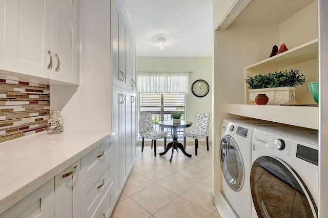 washroom featuring cabinets, washing machine and clothes dryer, light tile patterned floors, and a textured ceiling