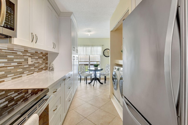 kitchen featuring tasteful backsplash, stainless steel appliances, white cabinetry, light tile patterned floors, and washing machine and clothes dryer