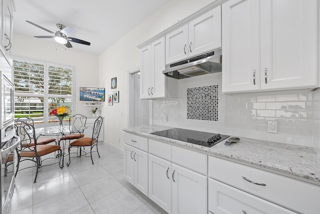 kitchen with light stone countertops, backsplash, black electric cooktop, white cabinetry, and light tile patterned floors