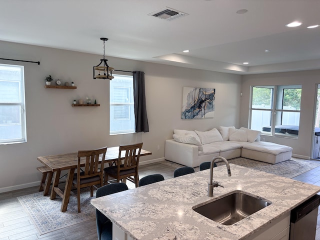 kitchen featuring pendant lighting, dark wood-type flooring, an inviting chandelier, sink, and light stone counters