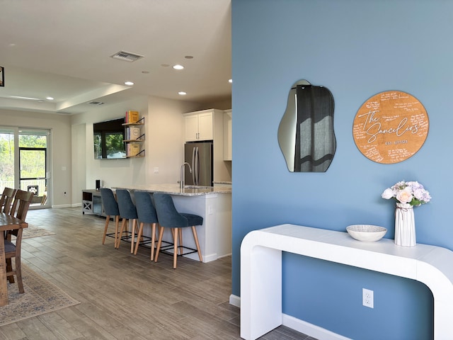 interior space featuring light stone counters, dark hardwood / wood-style floors, stainless steel fridge, a kitchen bar, and white cabinets