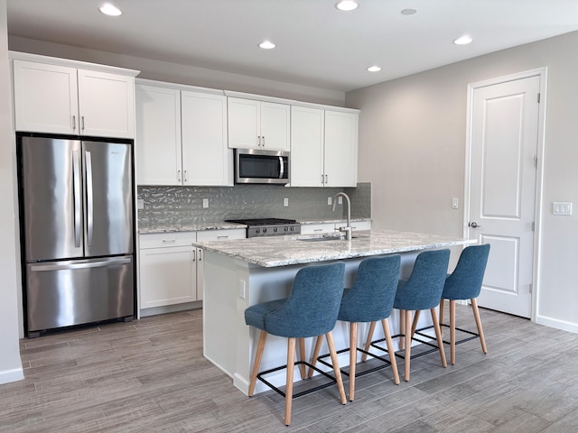 kitchen with white cabinets, light wood-type flooring, stainless steel appliances, and a kitchen island with sink