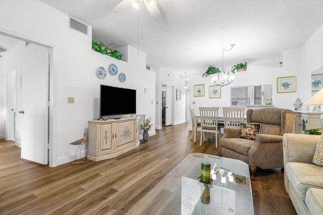 living room featuring ceiling fan with notable chandelier, wood-type flooring, and a textured ceiling