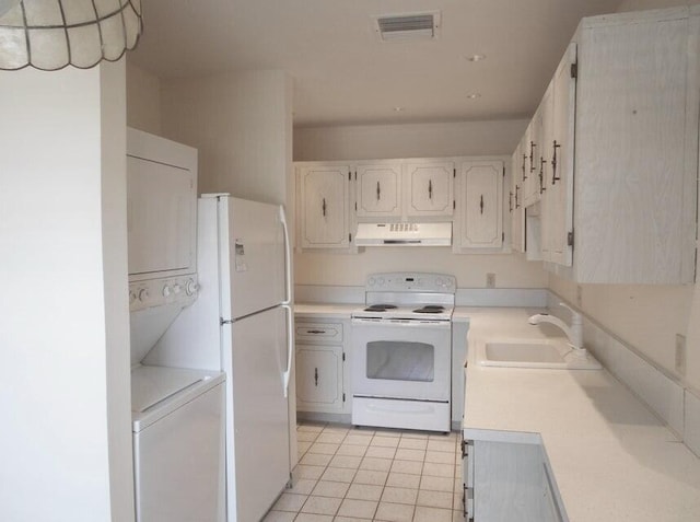 kitchen with white appliances, sink, white cabinets, light tile patterned floors, and stacked washer and clothes dryer