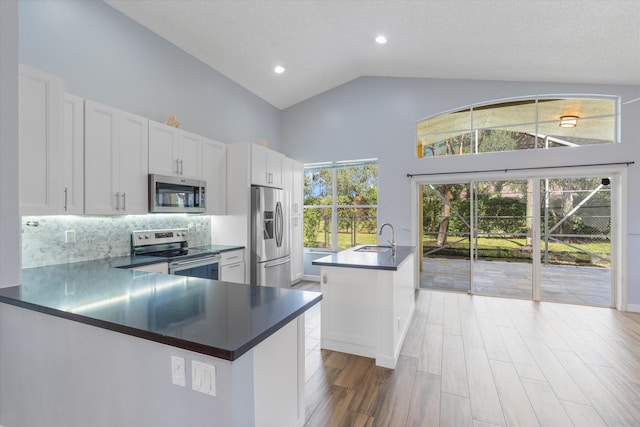 kitchen with white cabinets, stainless steel appliances, a center island with sink, and plenty of natural light