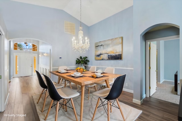 dining area with wood-type flooring, an inviting chandelier, and high vaulted ceiling