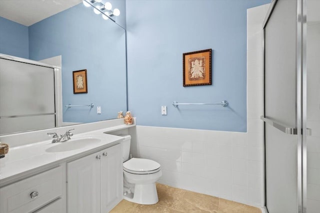 bathroom with tile patterned floors, toilet, vanity, tile walls, and an enclosed shower