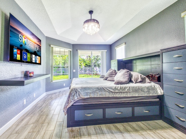 bedroom featuring a raised ceiling, a chandelier, a textured ceiling, and light wood-type flooring