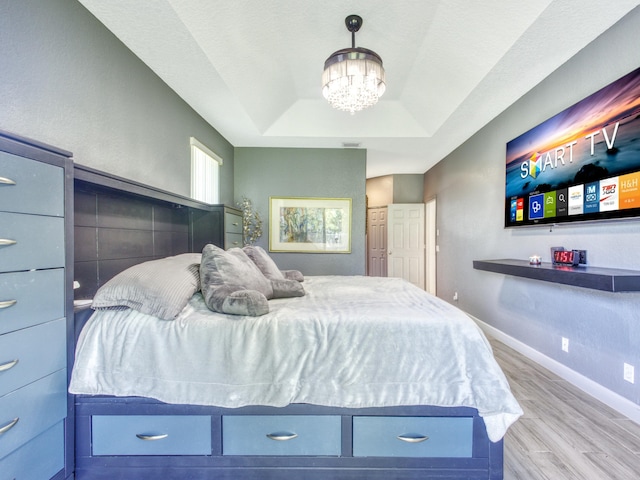 bedroom with a tray ceiling, light hardwood / wood-style flooring, and a chandelier