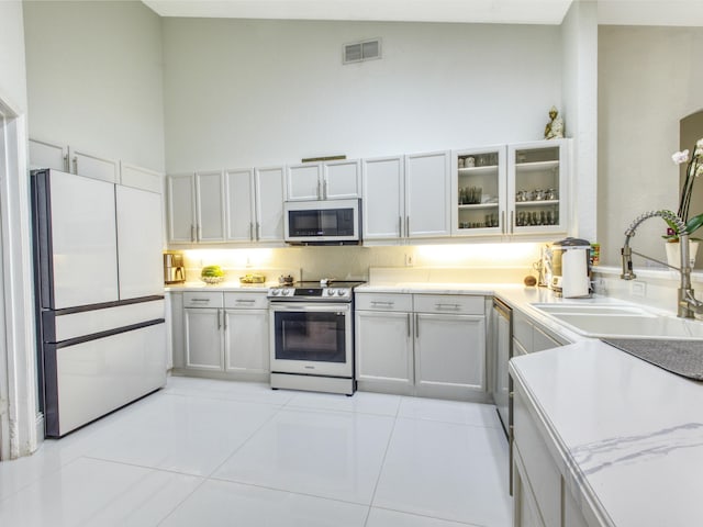 kitchen with sink, light tile patterned floors, stainless steel appliances, and high vaulted ceiling