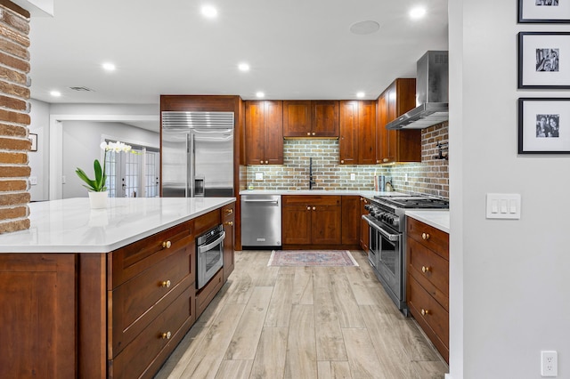 kitchen featuring sink, wall chimney exhaust hood, high end appliances, light wood-type flooring, and decorative backsplash