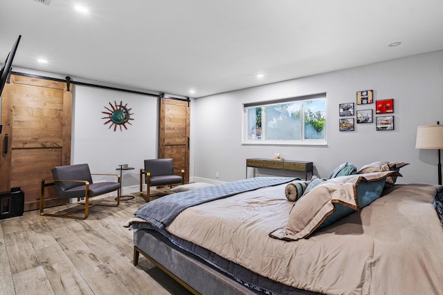 bedroom with a barn door and light hardwood / wood-style floors