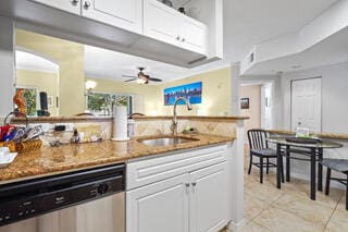 kitchen featuring ceiling fan, dishwasher, sink, dark stone counters, and white cabinets