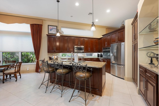 kitchen featuring pendant lighting, appliances with stainless steel finishes, an island with sink, and light stone countertops