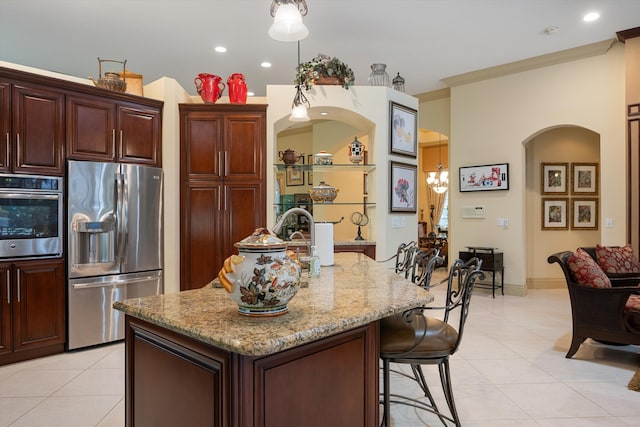 kitchen featuring light tile patterned floors, a kitchen island with sink, crown molding, light stone countertops, and appliances with stainless steel finishes