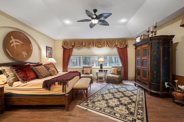 bedroom with a textured ceiling, a raised ceiling, vaulted ceiling, dark wood-type flooring, and ceiling fan