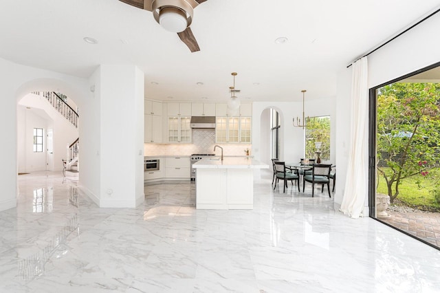 kitchen with white cabinetry, tasteful backsplash, hanging light fixtures, an island with sink, and high end stainless steel range oven